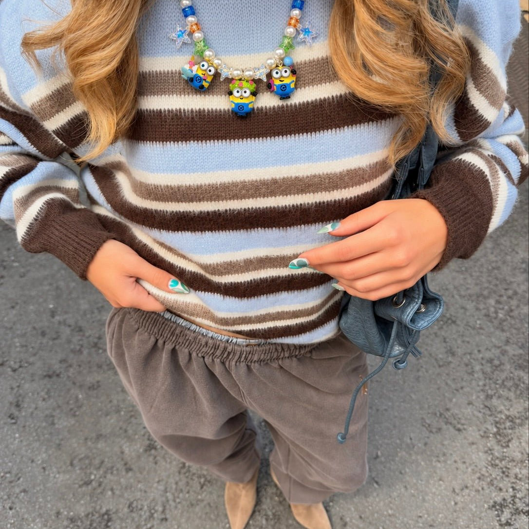 Overhead view of a model wearing a pearl and colorful crystal necklace with three yellow goggled figure charms over a striped sweater.