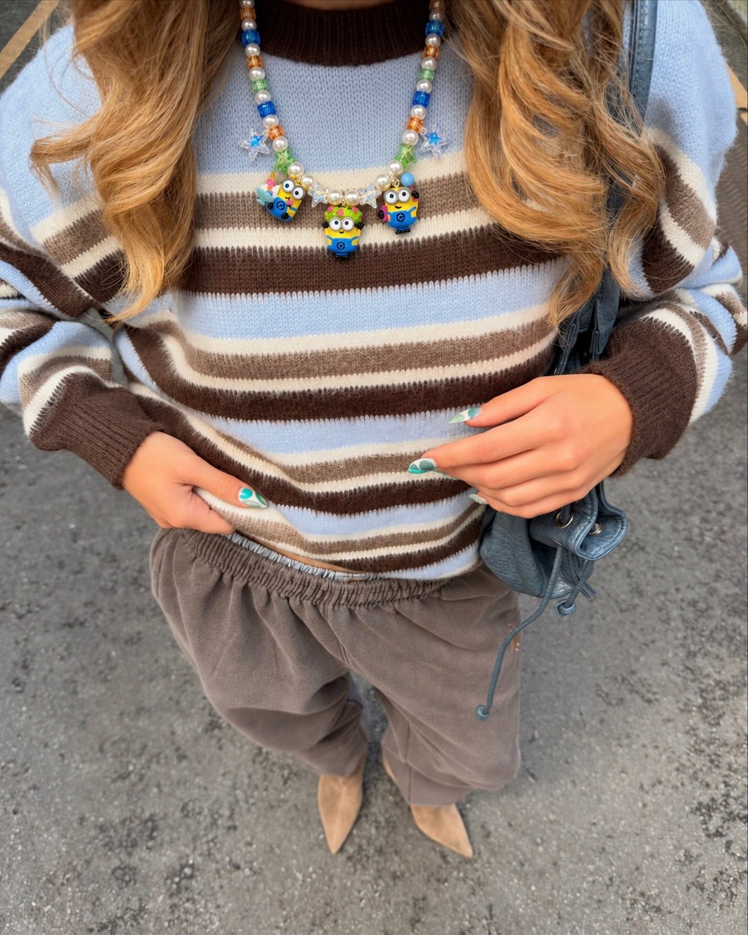 Overhead view of a model wearing a pearl and colorful crystal necklace with three yellow goggled figure charms over a striped sweater.