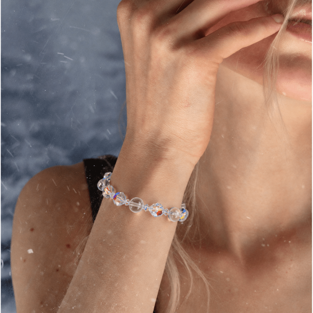 Aurora Crystal Bracelet with clear iridescent round beads, worn on a raised wrist beside a black top.