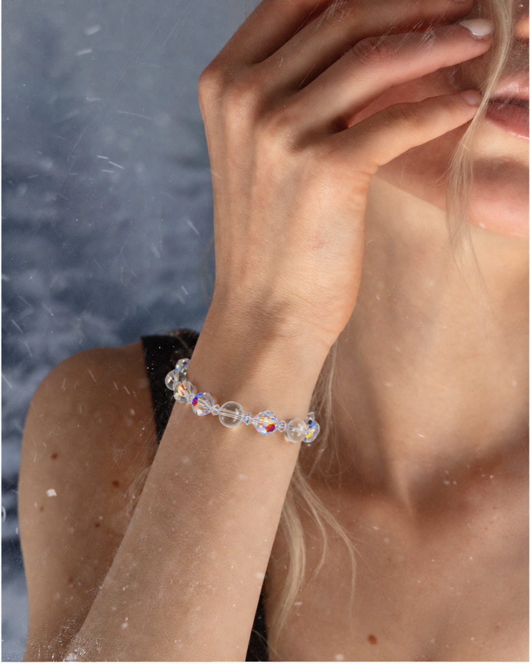 Aurora Crystal Bracelet with clear iridescent round beads, worn on a raised wrist beside a black top.
