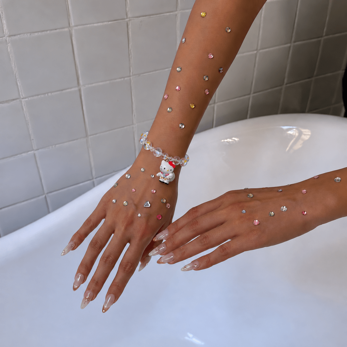 Iridescent crystal bracelet with a white cat charm worn on a wrist decorated with colorful rhinestones.