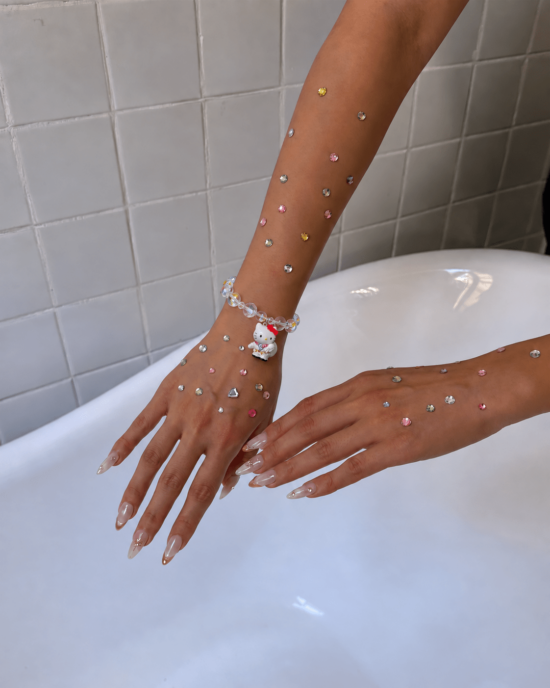 Iridescent crystal bracelet with a white cat charm worn on a wrist decorated with colorful rhinestones.