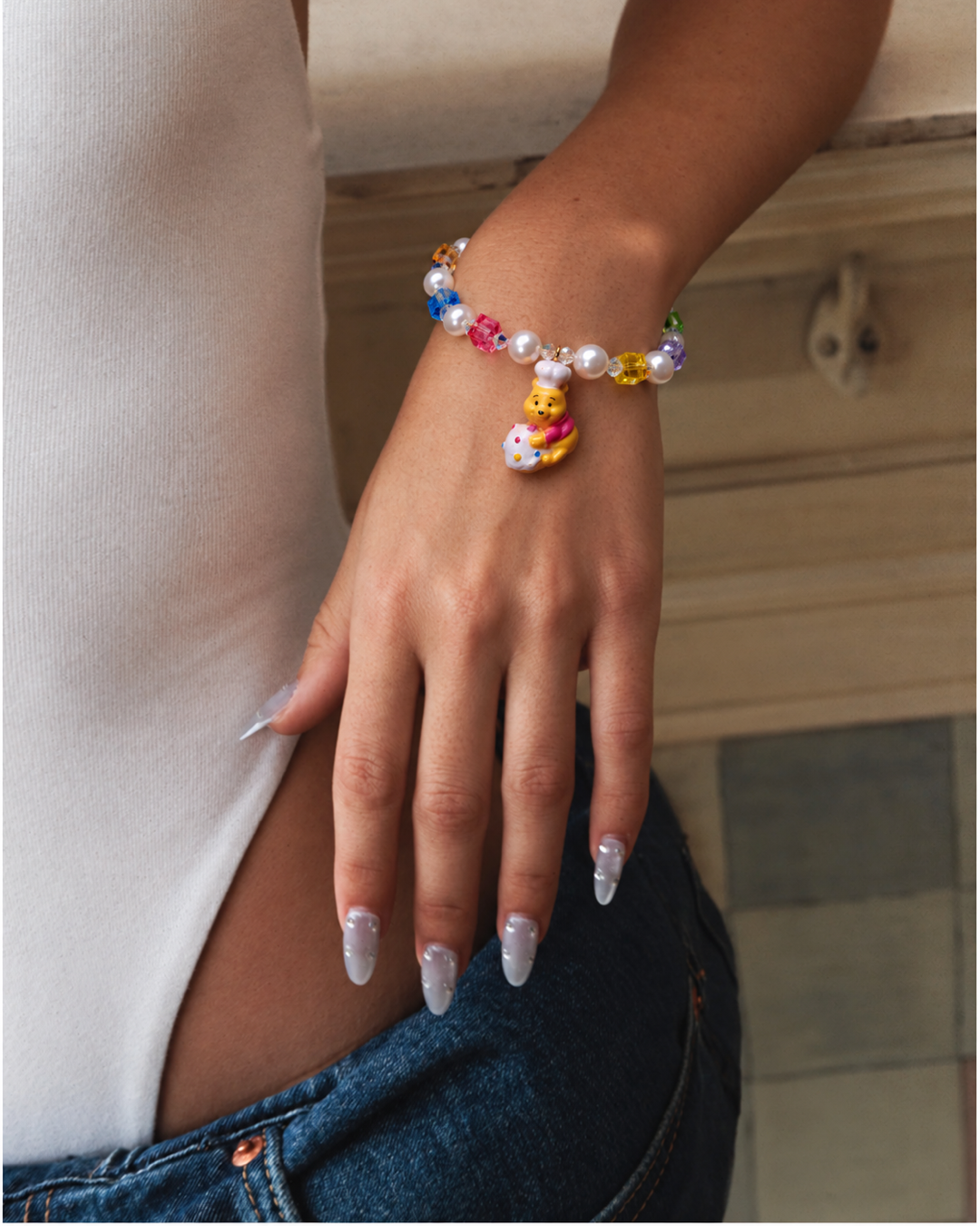Honey Baker Charm Bracelet with rainbow crystal cubes, white pearls and a bear chef charm, worn with a white top and jeans.