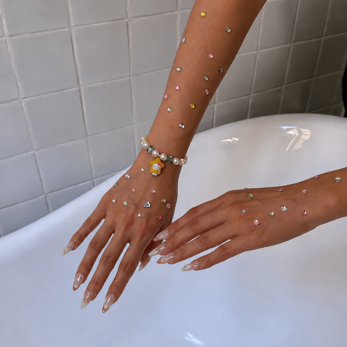 Crystal pearl bracelet with green and champagne crystals and a yellow star cat charm, worn on a hand decorated with rhinestones.