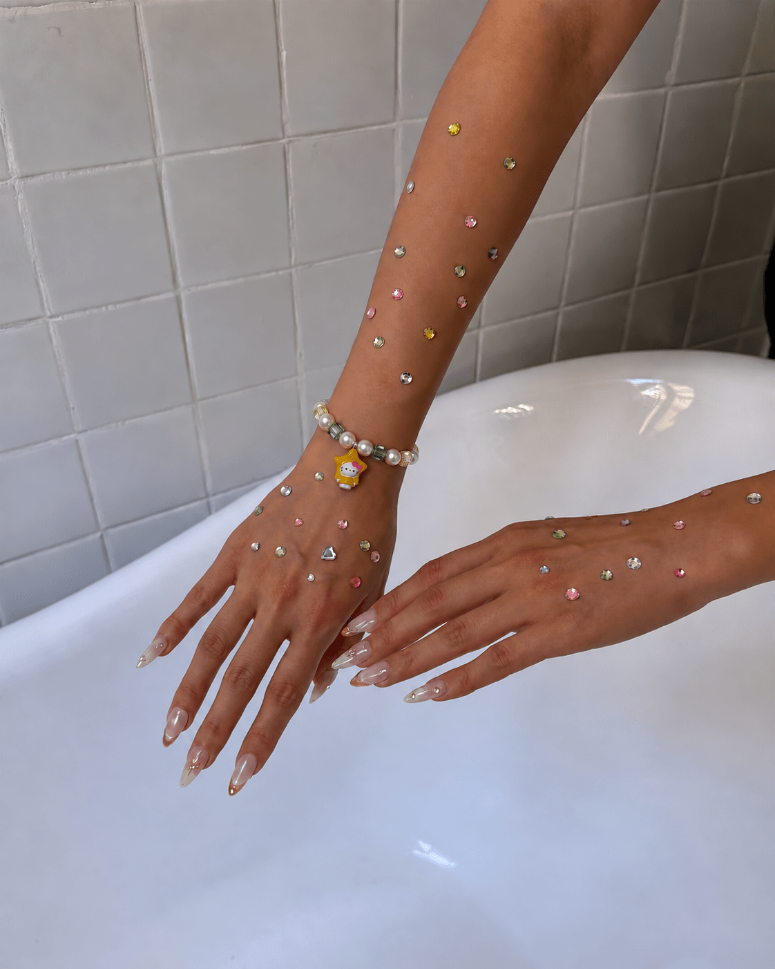 Crystal pearl bracelet with green and champagne crystals and a yellow star cat charm, worn on a hand decorated with rhinestones.