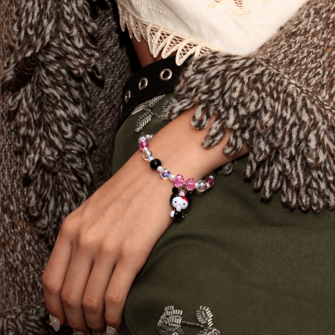Pink Bow Midnight Cat Charm Bracelet with pink, black and iridescent beads, worn beside a brown cardigan and olive-green clothing.