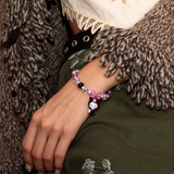 Pink Bow Midnight Cat Charm Bracelet with pink, black and iridescent beads, worn beside a brown cardigan and olive-green clothing.