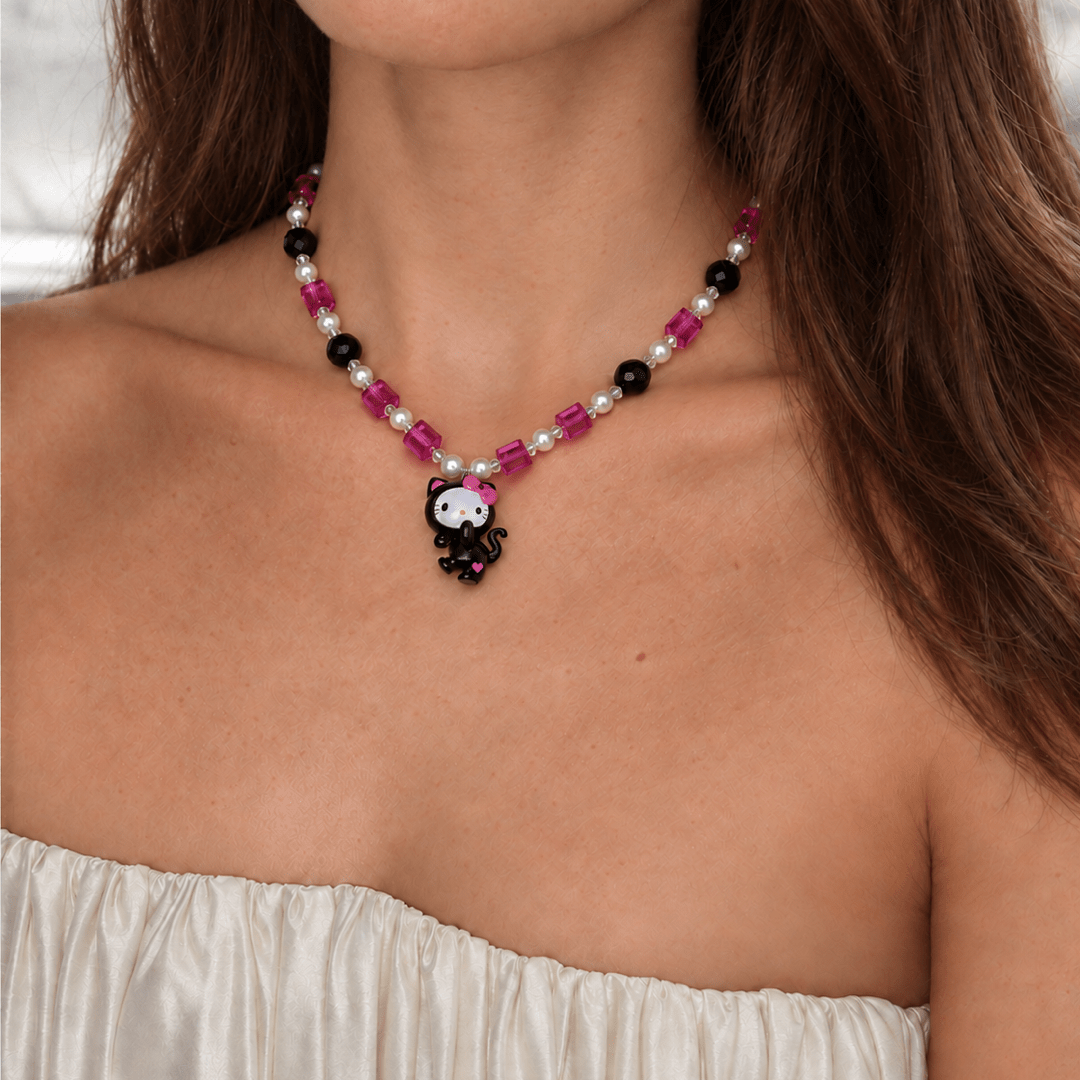 Pink Noir Cat Charm Necklace with pink crystals, black beads and white pearls, worn with a white ruched strapless top.