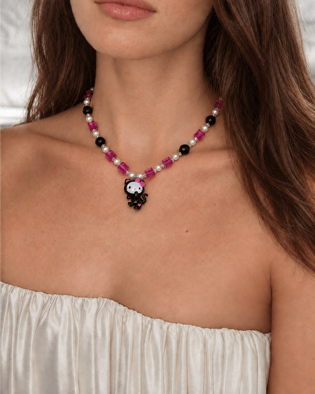 Pink Noir Cat Charm Necklace with pink crystals, black beads and white pearls, worn with a white ruched strapless top.