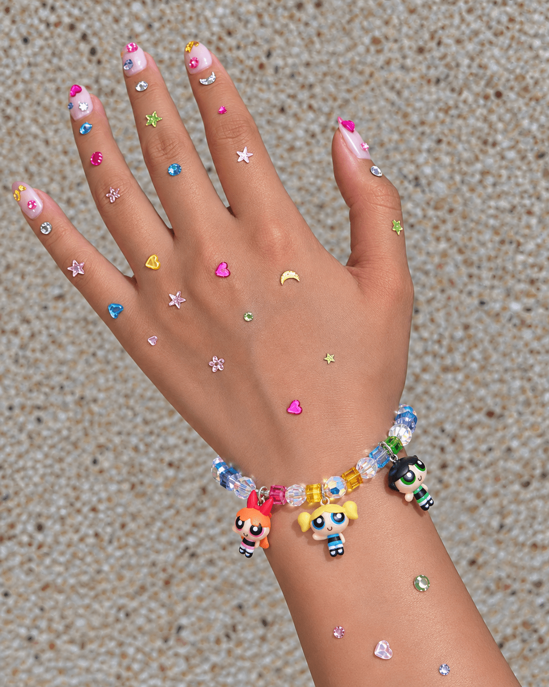 Close-up of a rainbow crystal bracelet with three colorful character charms on a wrist decorated with tiny gems.