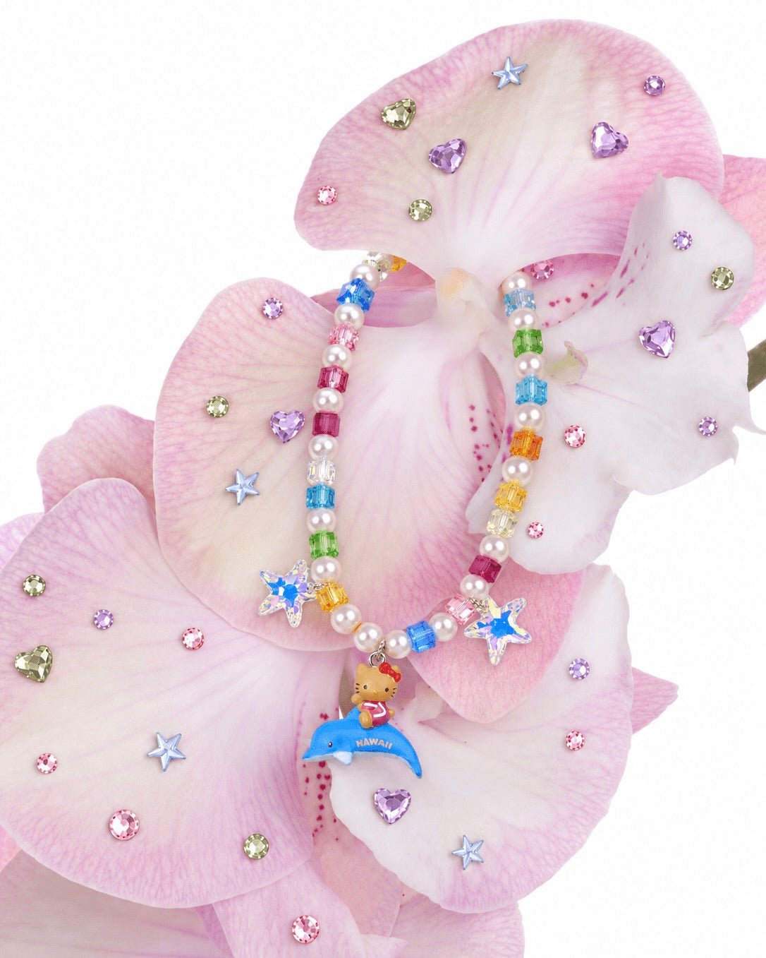 Rainbow crystal and pearl necklace with blue stars and a cat riding a dolphin, draped over pink orchids.