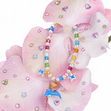 Rainbow crystal and pearl necklace with blue stars and a cat riding a dolphin, draped over pink orchids.