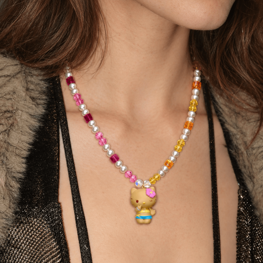 Tropical Sunshine Charm Necklace with pink and golden crystals, white pearls and a flower-wearing cat pendant, worn with a black top.