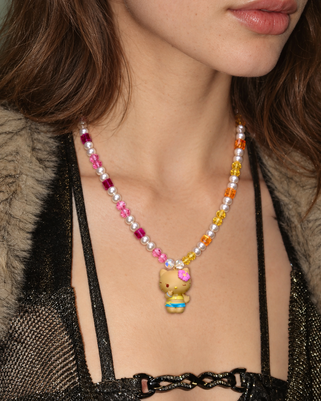 Tropical Sunshine Charm Necklace with pink and golden crystals, white pearls and a flower-wearing cat pendant, worn with a black top.