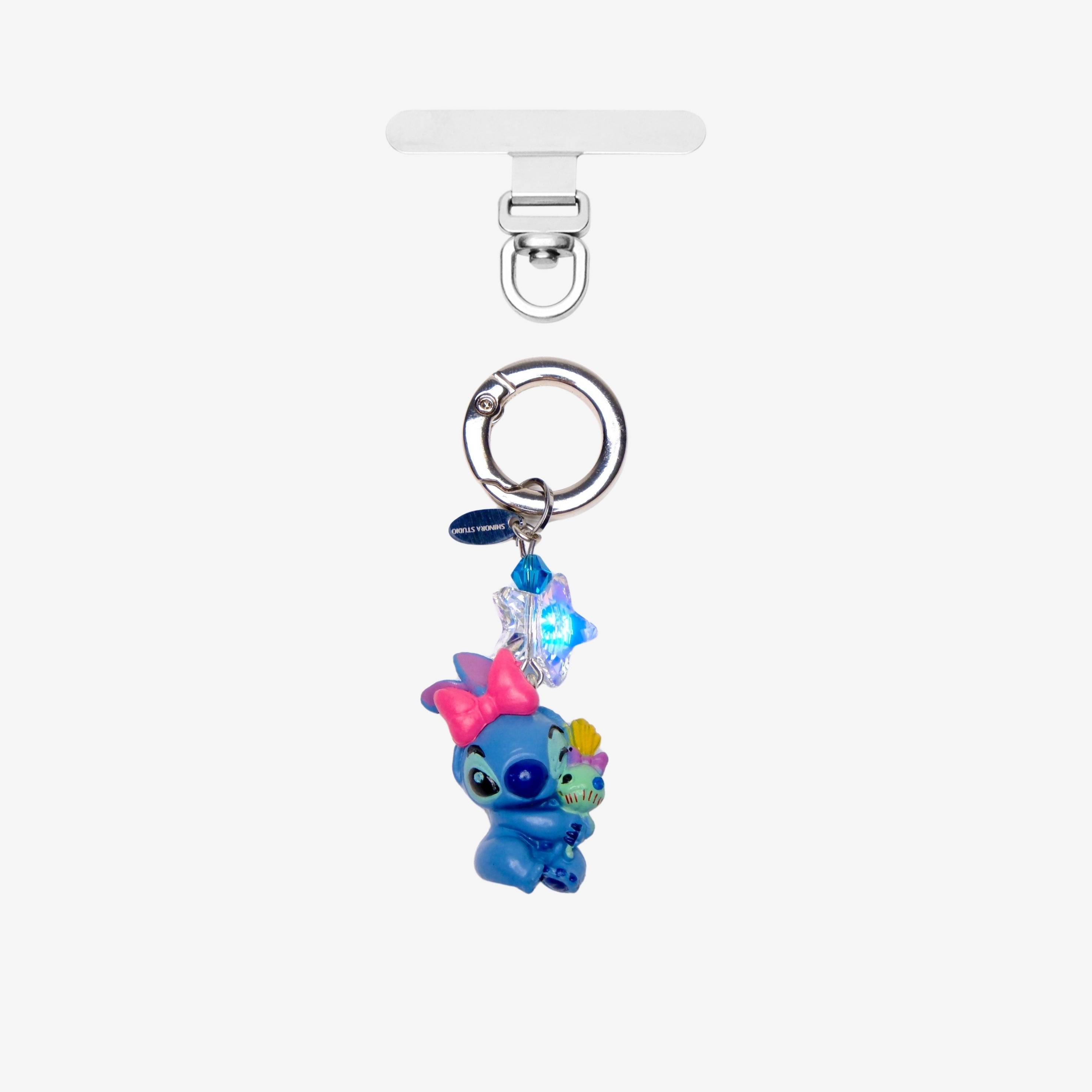 Detachable phone charm with a blue creature wearing a pink bow, a smaller colorful figure, blue crystals and a silver-tone ring.