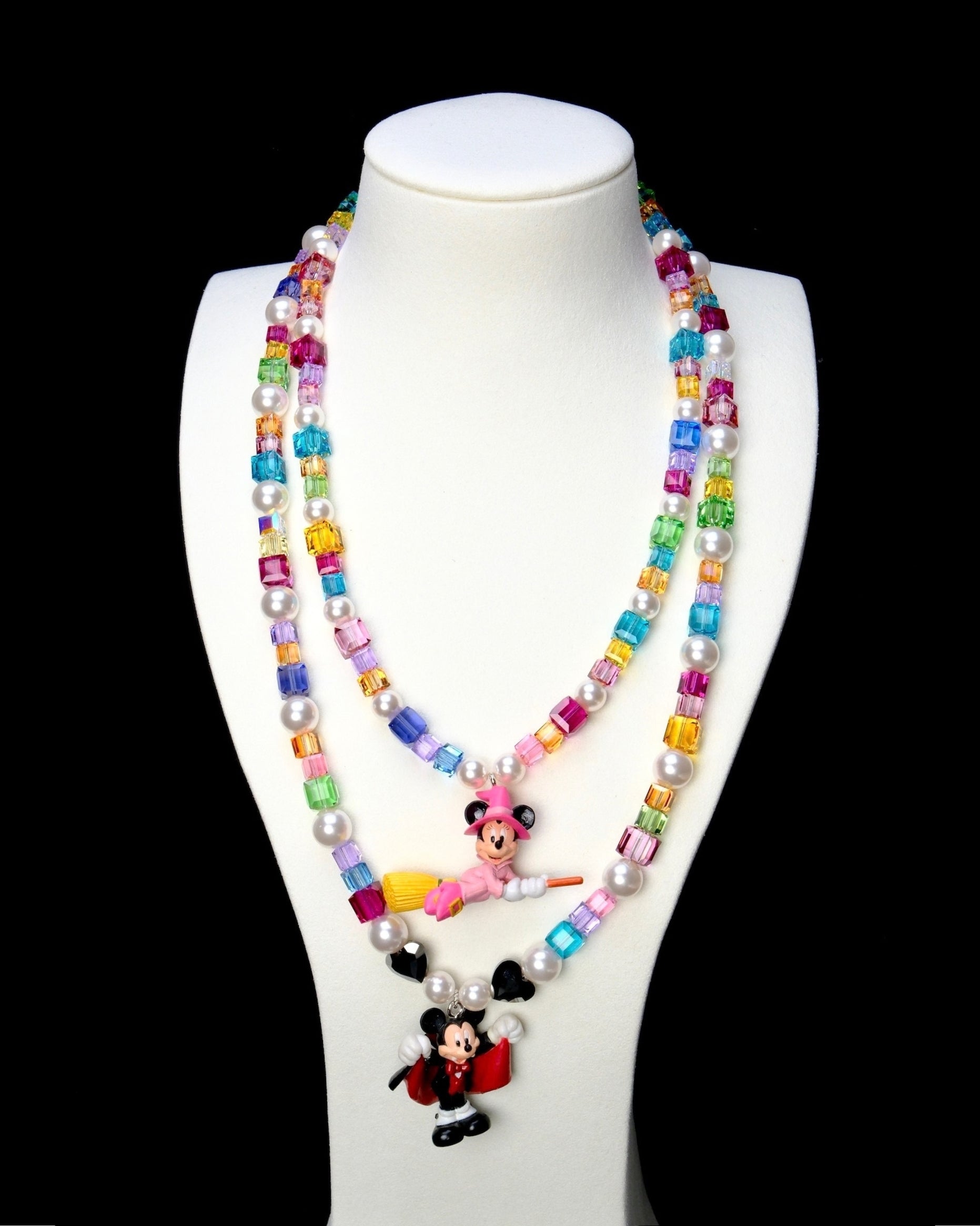 Rainbow crystal and pearl witch mouse necklace layered above a red-caped vampire mouse necklace on a white bust.