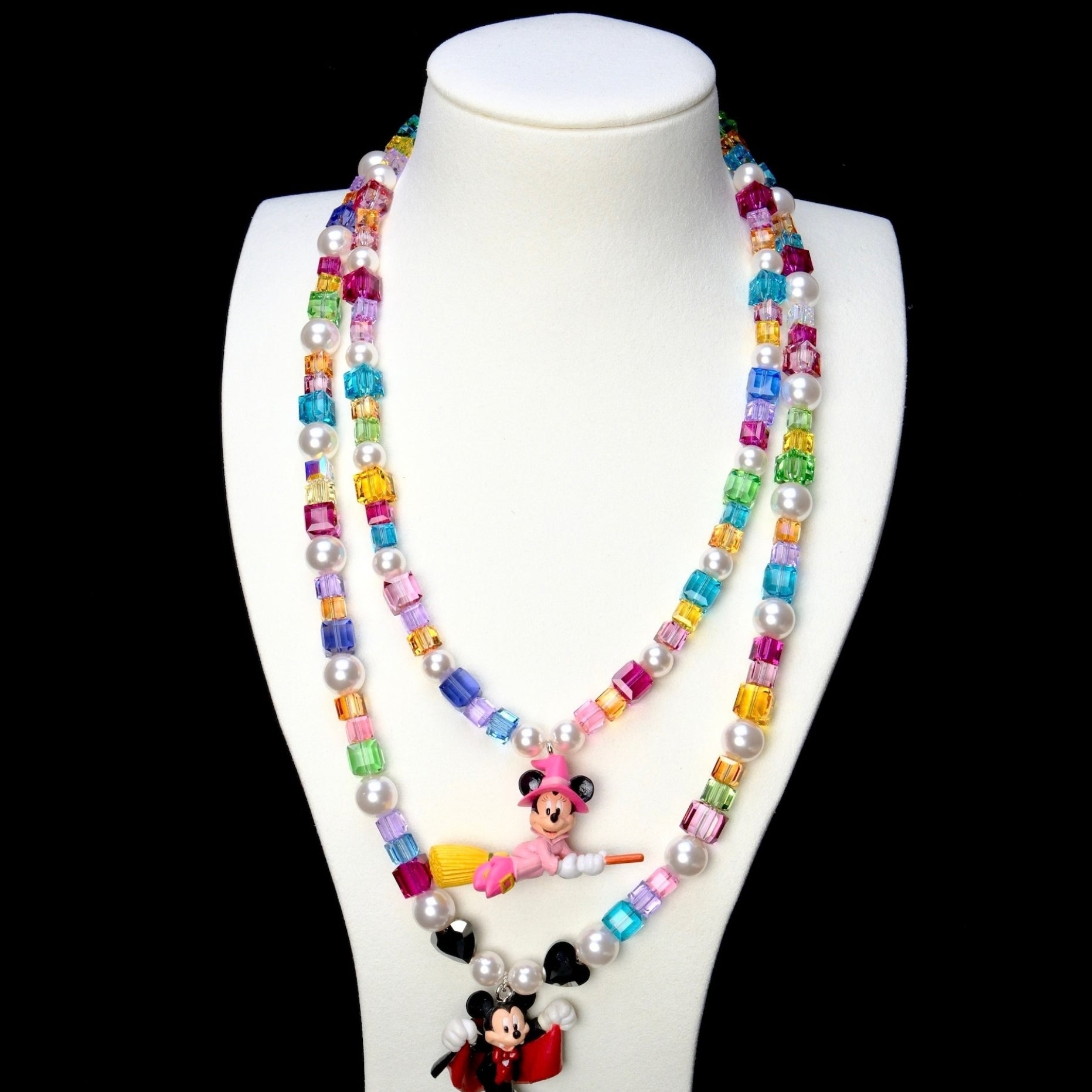 Rainbow crystal and pearl vampire mouse necklace layered below a pink witch mouse necklace on a white bust.