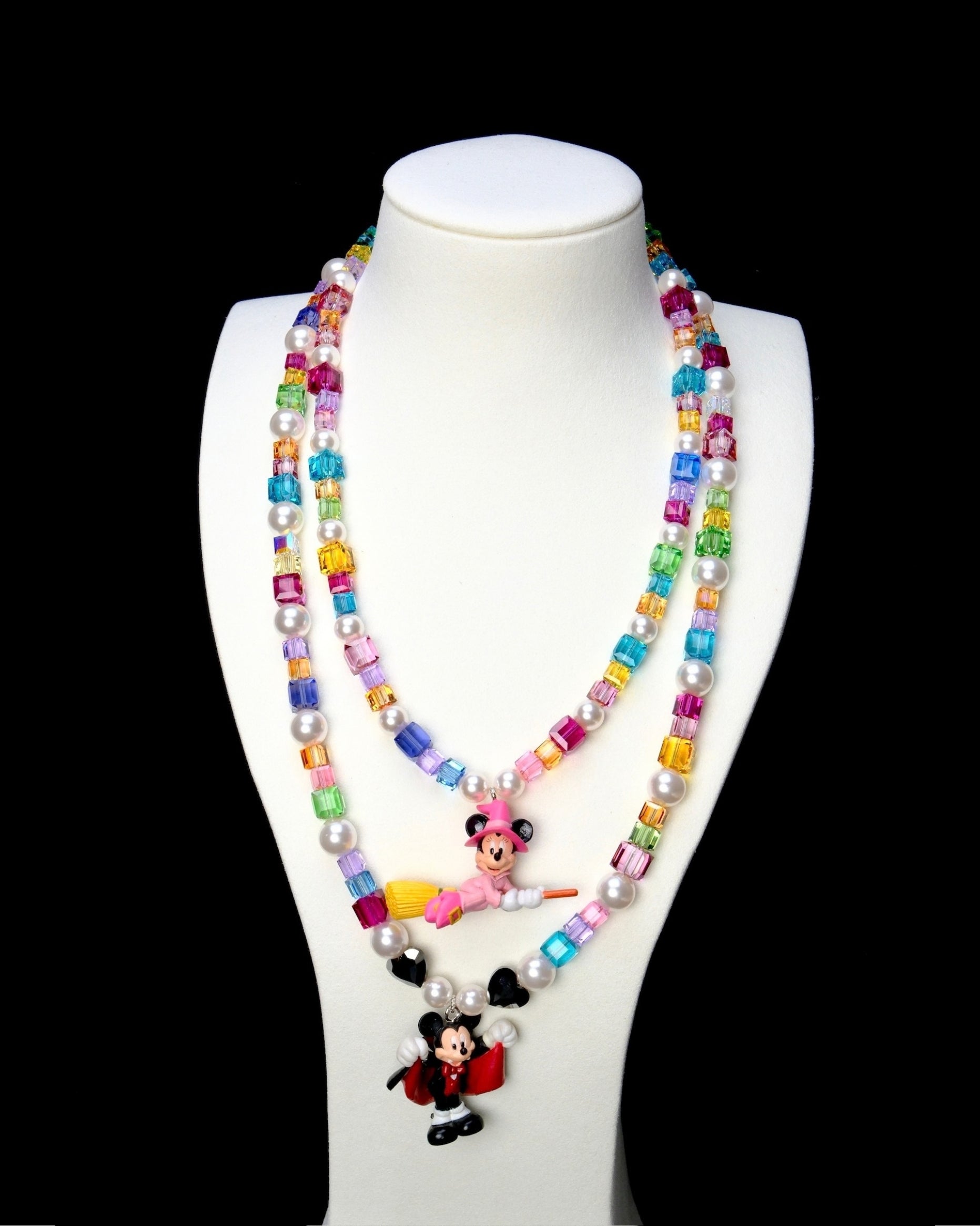 Rainbow crystal and pearl vampire mouse necklace layered below a pink witch mouse necklace on a white bust.