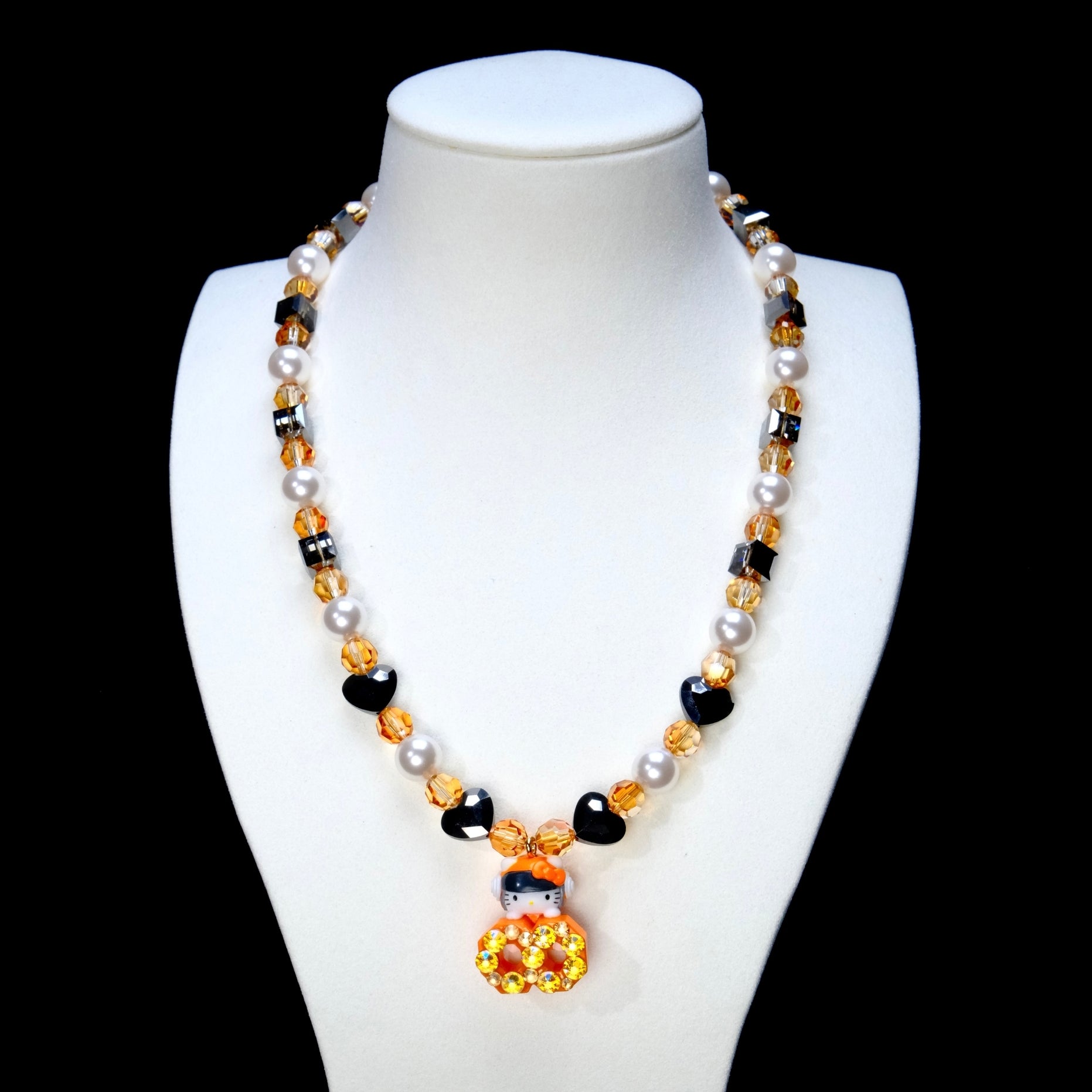 Amber crystal and white pearl necklace with black heart beads and an orange jeweled cat charm on a white display bust.