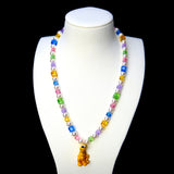 Rainbow crystal cube and white pearl necklace with a yellow dog charm, displayed on a white bust against black.