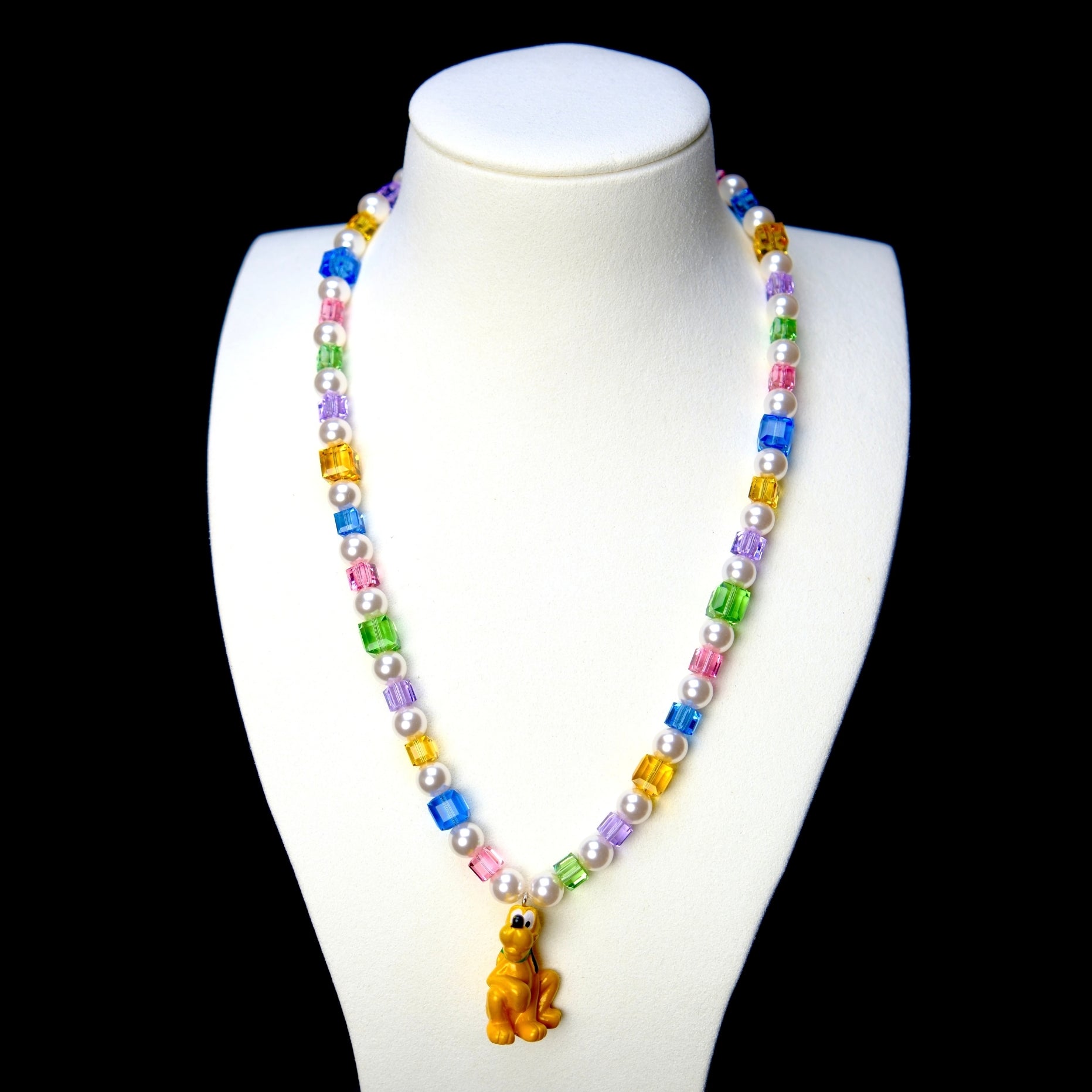 Rainbow crystal cube and white pearl necklace with a yellow dog charm, displayed on a white bust against black.