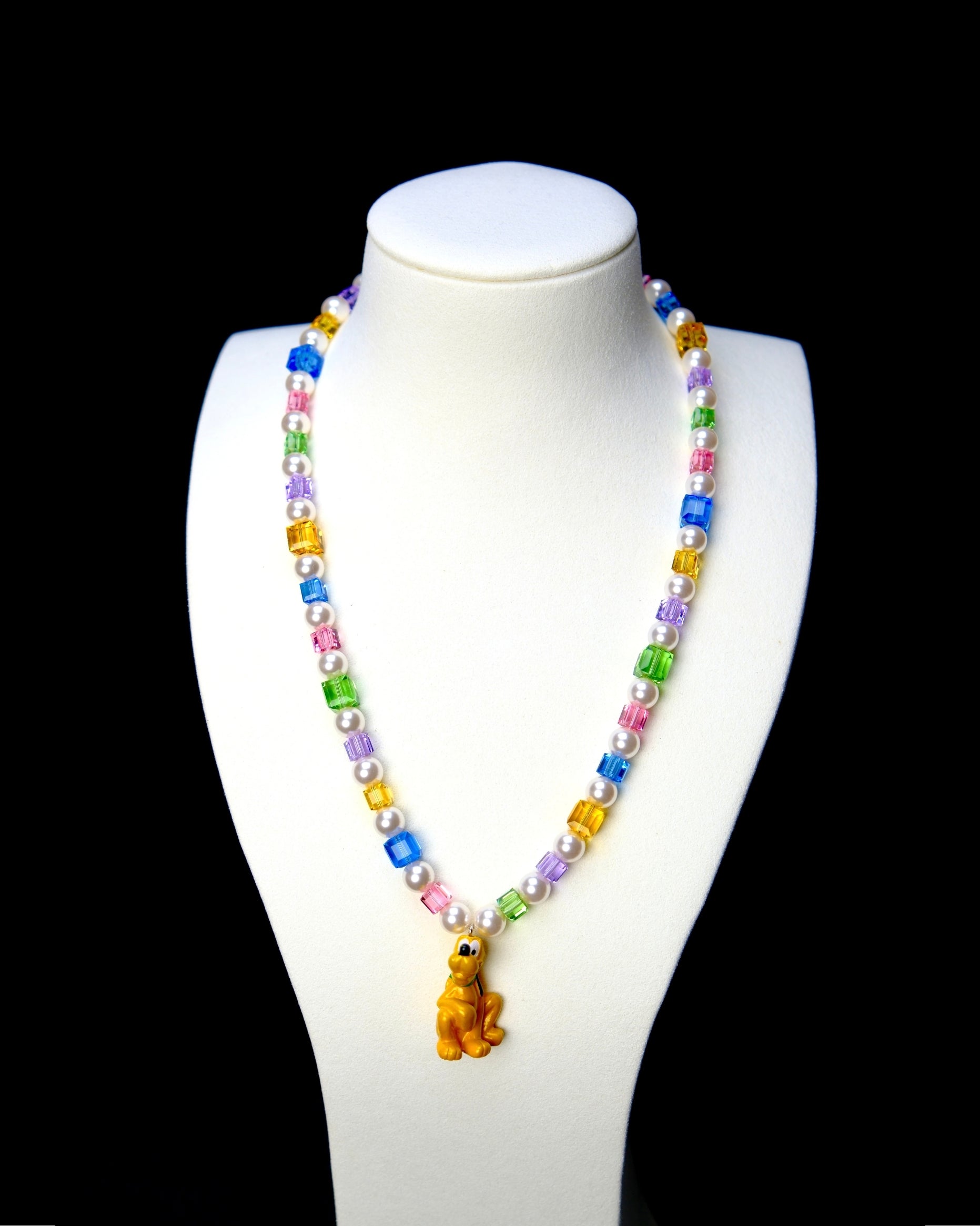 Rainbow crystal cube and white pearl necklace with a yellow dog charm, displayed on a white bust against black.