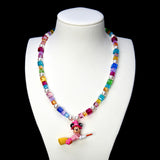 Rainbow crystal and white pearl necklace with a pink witch mouse riding a broom, displayed on a white bust against black.