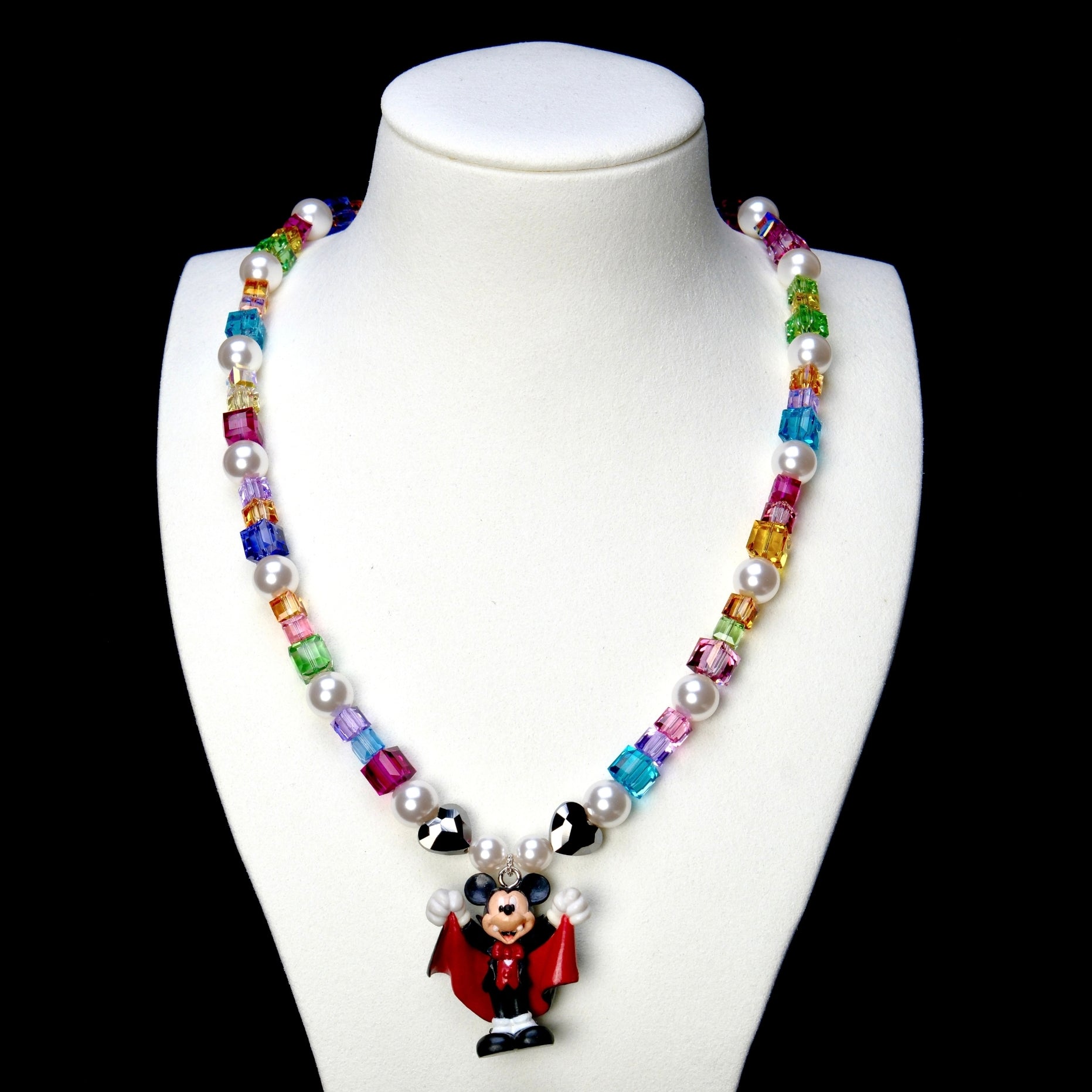 Rainbow crystal and white pearl necklace with black hearts and a red-caped vampire mouse charm, displayed on a white bust.