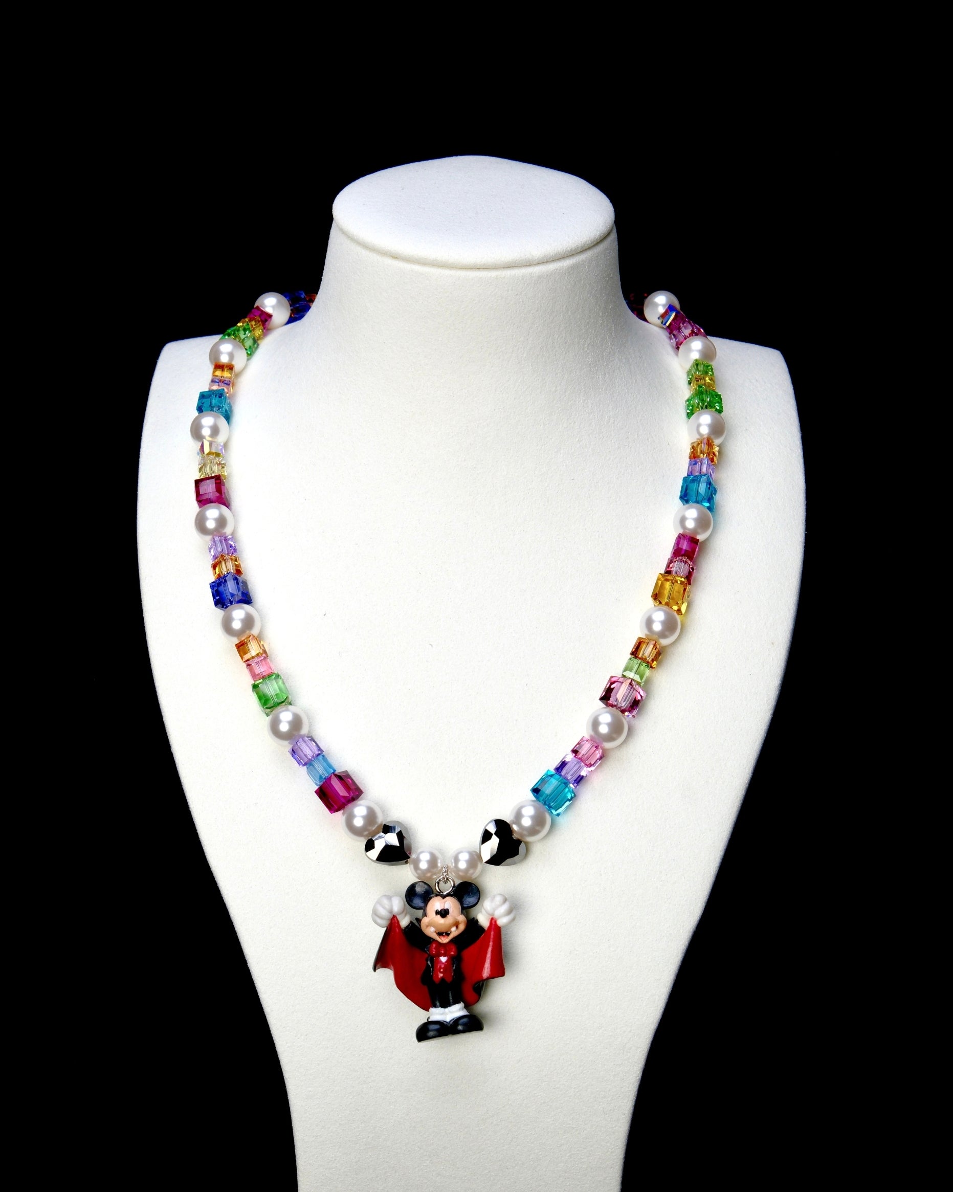 Rainbow crystal and white pearl necklace with black hearts and a red-caped vampire mouse charm, displayed on a white bust.