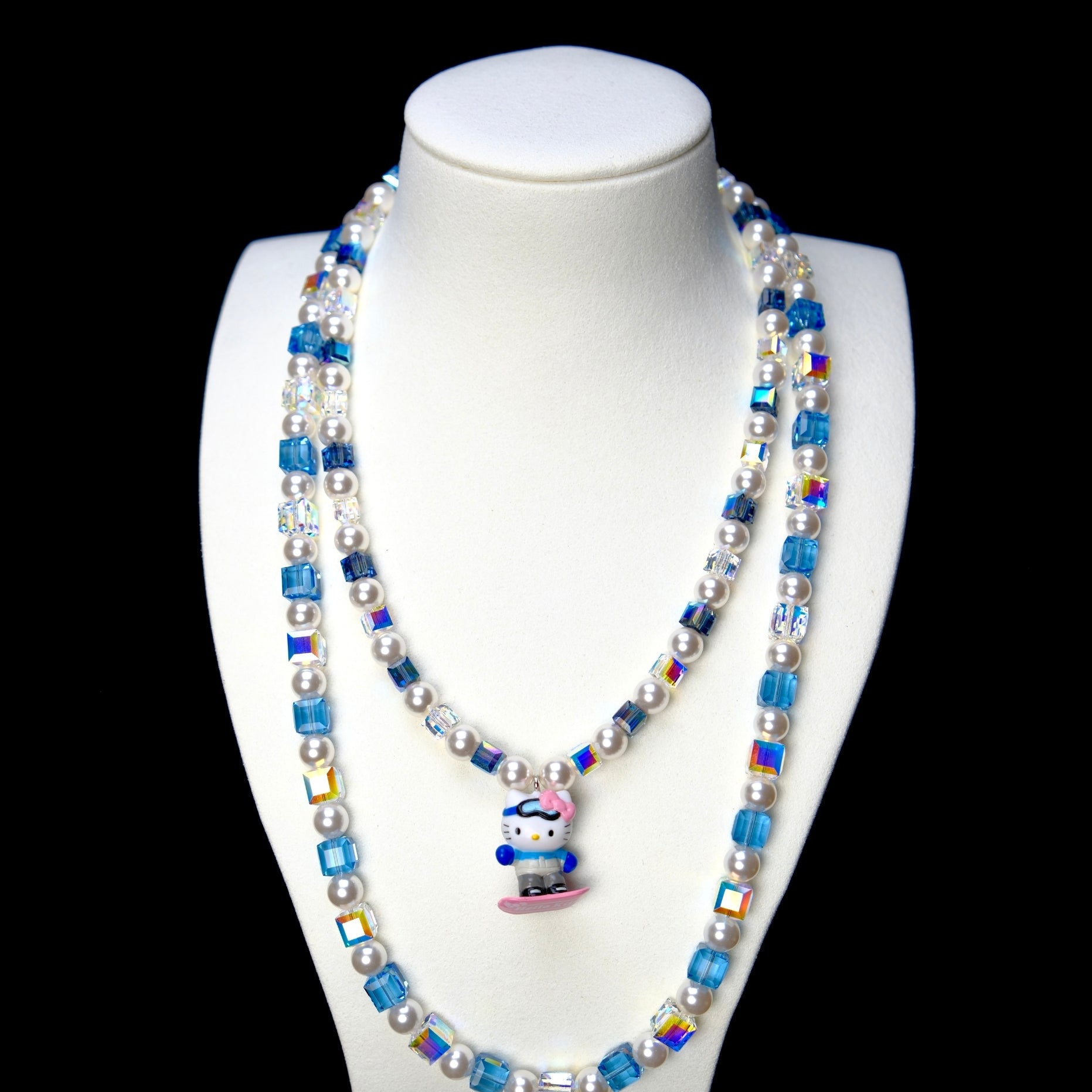 Blue and clear crystal double-layer necklace with white pearls and a snowboard cat charm, displayed on a white bust.