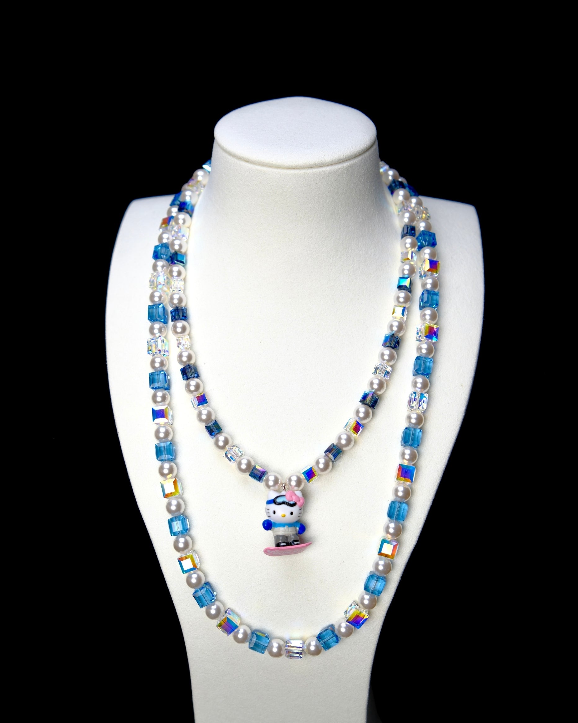 Blue and clear crystal double-layer necklace with white pearls and a snowboard cat charm, displayed on a white bust.