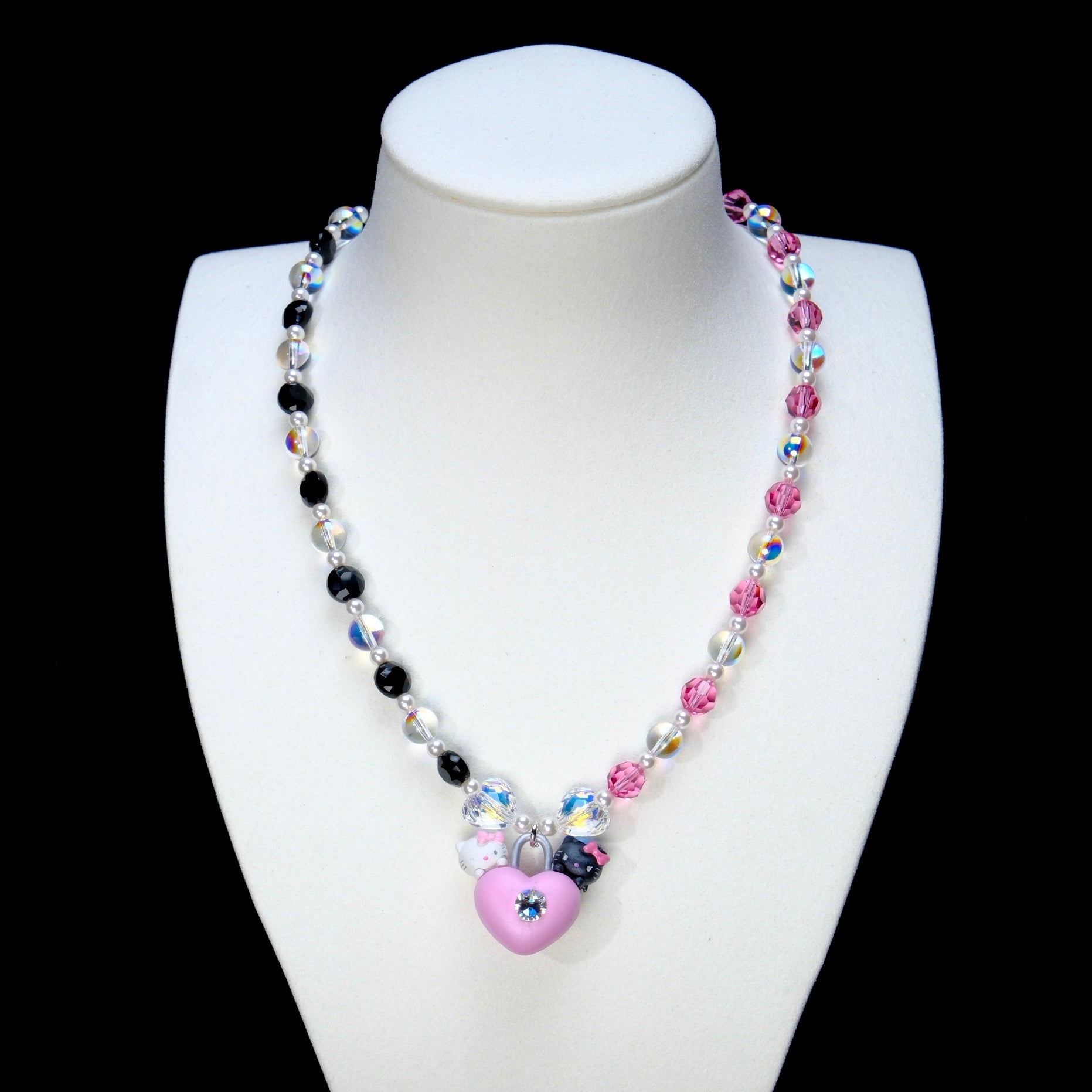 Pink and black crystal necklace with small pearl accents and a pink heart-lock pendant on a white display bust.