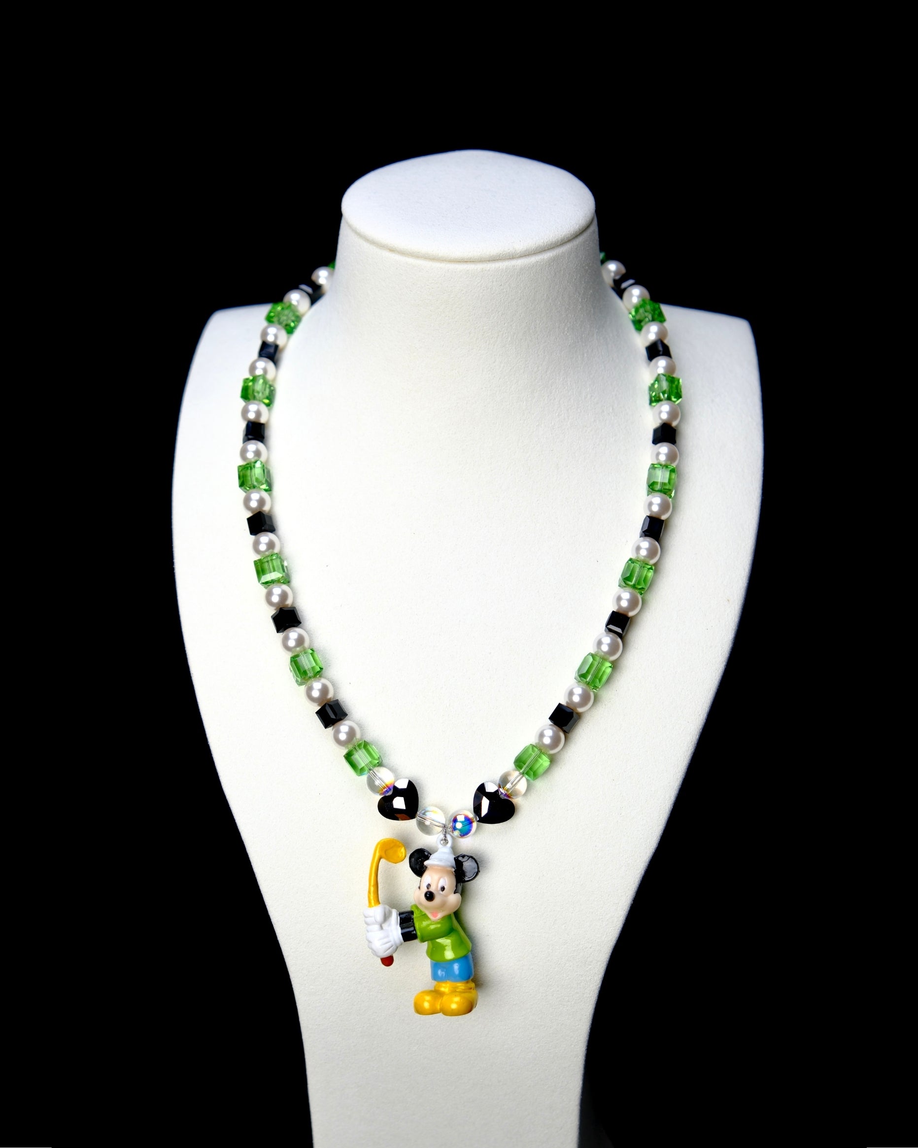 Green crystal and white pearl necklace with black heart beads and a sporty mouse charm, displayed on a white bust.