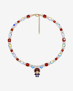 Amber-brown crystal and white pearl necklace with iridescent star beads, a bonnet-wearing doll charm and extension chain laid flat.