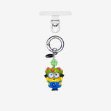 Yellow goggle-eyed character phone charm wearing a floral crown, with a green crystal accent and silver attachment ring.