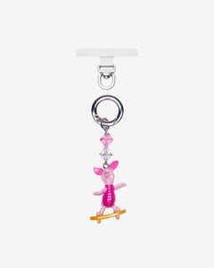 Detachable phone charm with a pink animal figure on a yellow skateboard, pink crystal accents and a silver-tone ring.