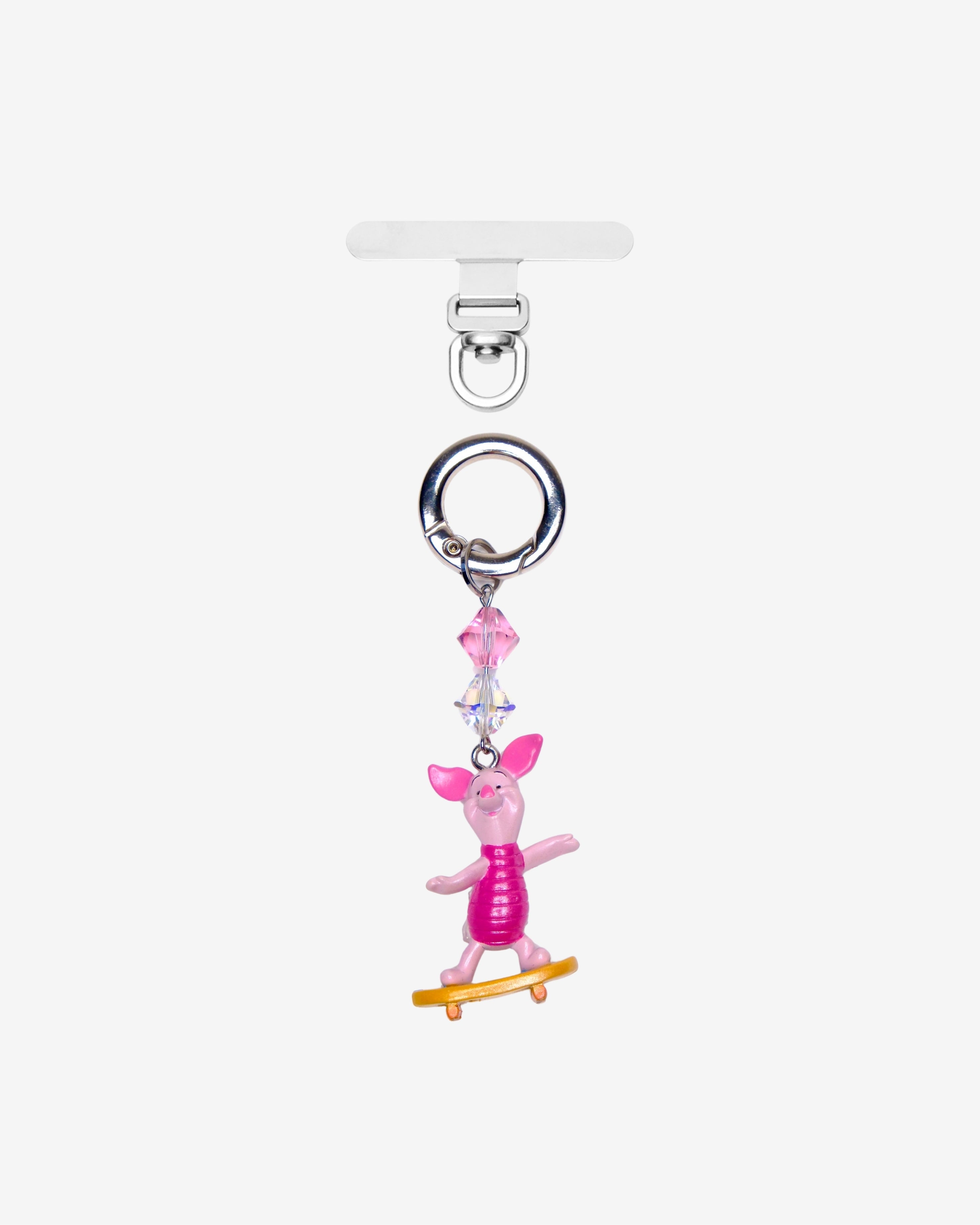 Detachable phone charm with a pink animal figure on a yellow skateboard, pink crystal accents and a silver-tone ring.