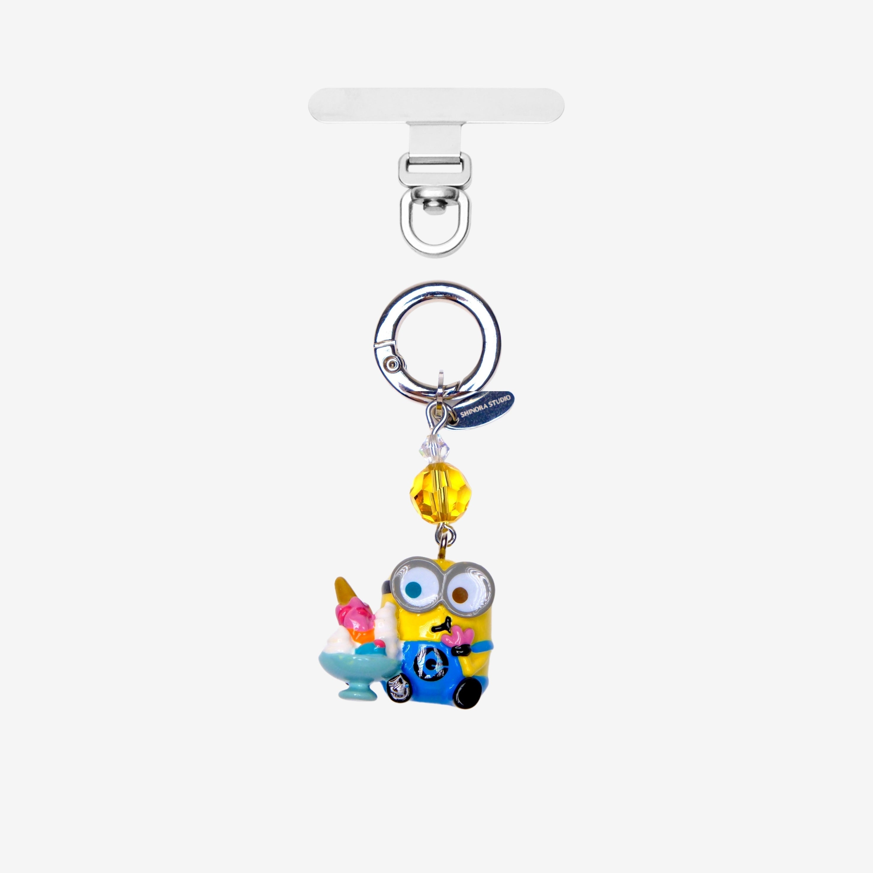 Yellow goggle-eyed character phone charm holding a sundae, with a yellow crystal accent and silver attachment ring.