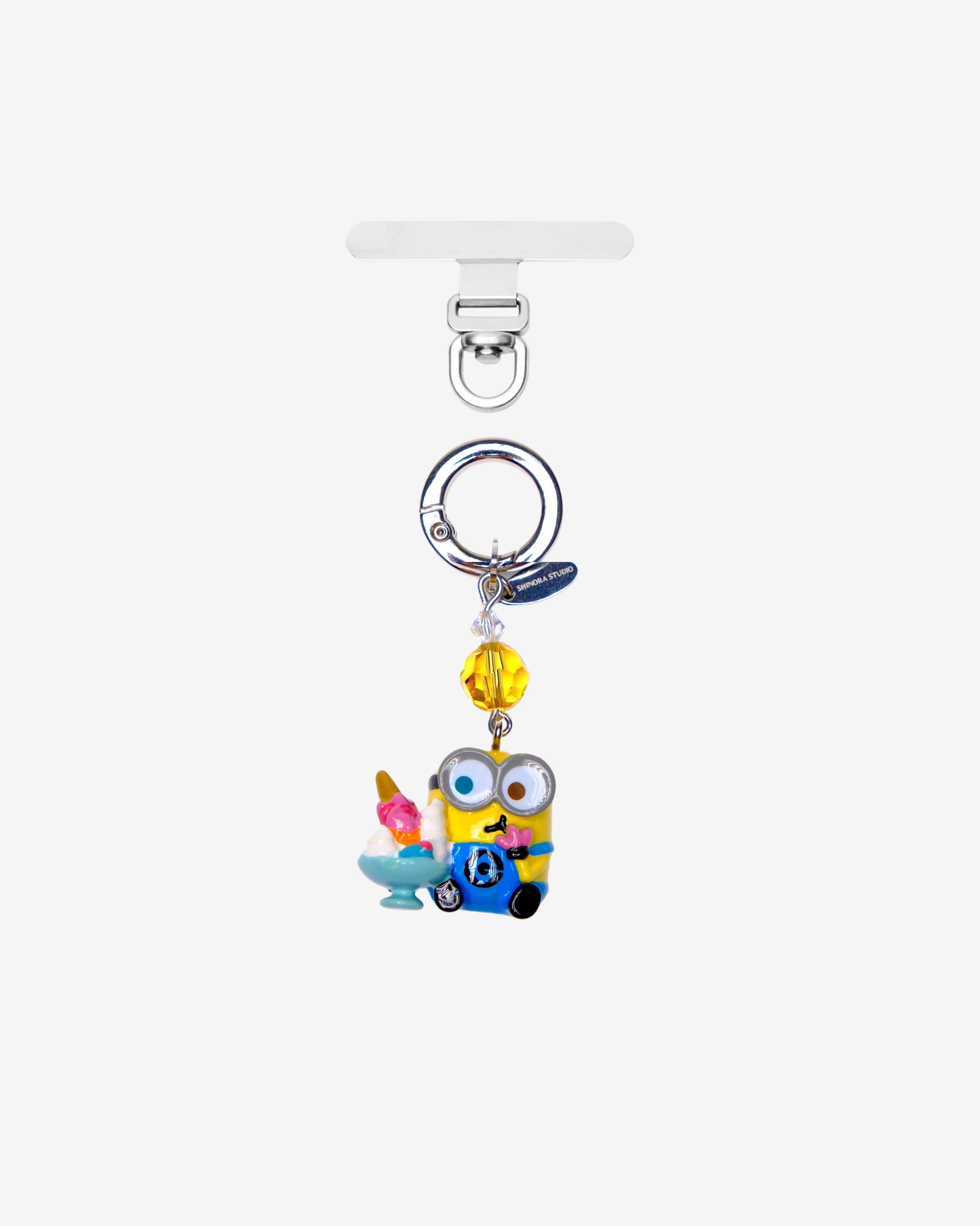 Yellow goggle-eyed character phone charm holding a sundae, with a yellow crystal accent and silver attachment ring.