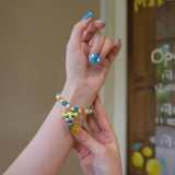 Wrist view of a handmade blue Swarovski crystal charm bracelet with pearls and playful charm details.
