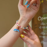 Wrist view of a handmade colorful Swarovski crystal charm bracelet with pearls and playful charm details.