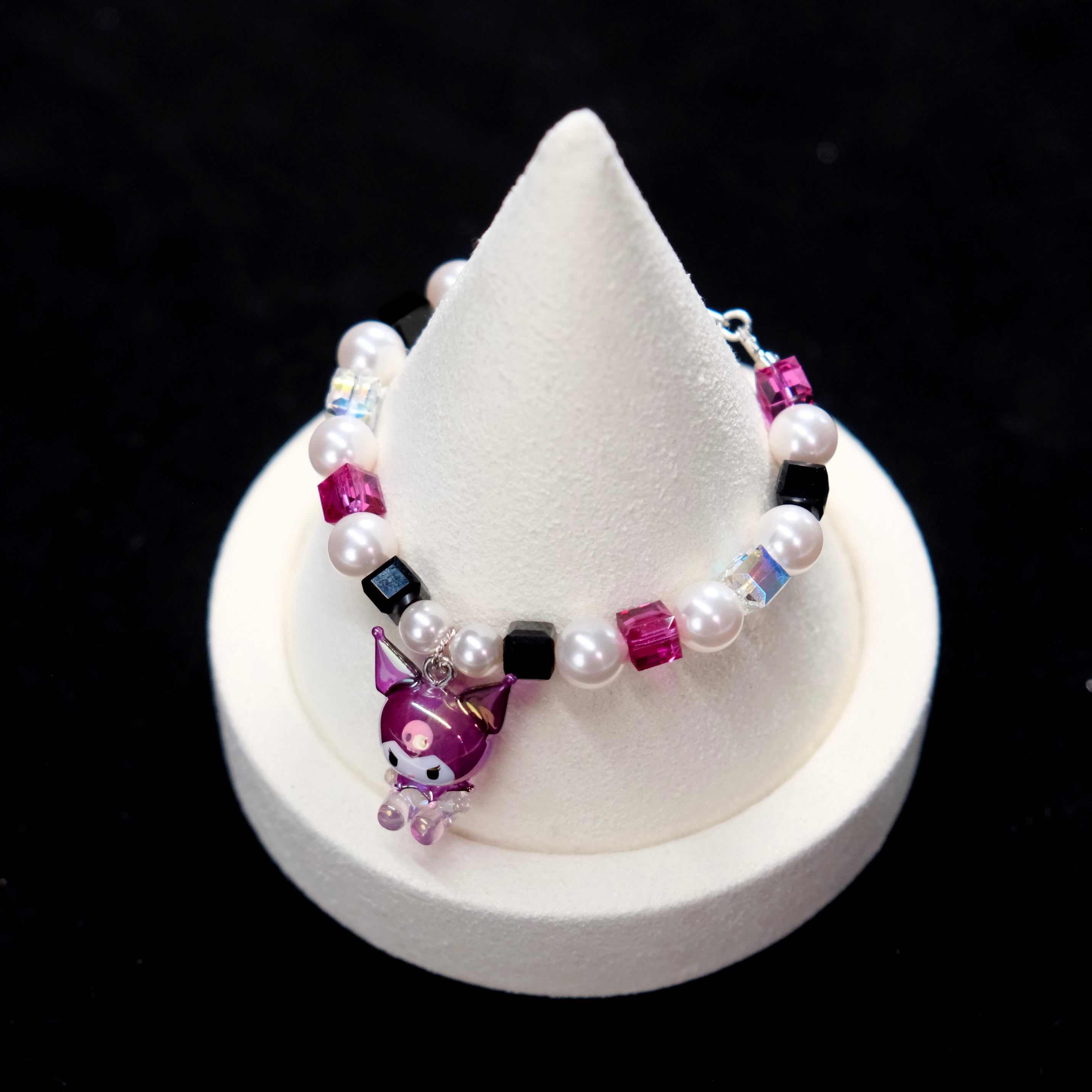 Wrist view of a handmade purple Swarovski crystal charm bracelet with pearls and playful charm details.