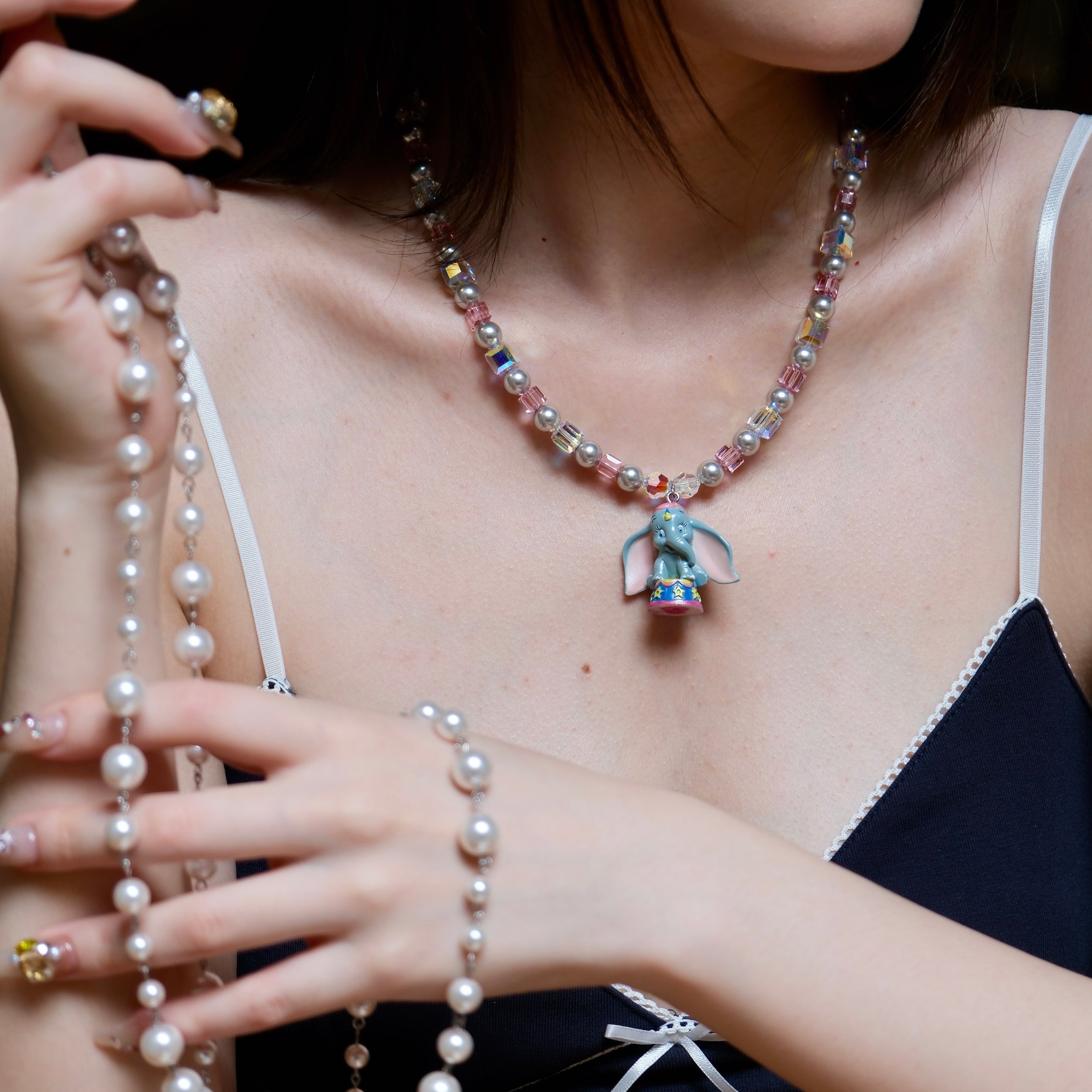 Close-up of a handmade blue elephant charm necklace with gray Swarovski pearls, pink beads, and iridescent crystal accents.