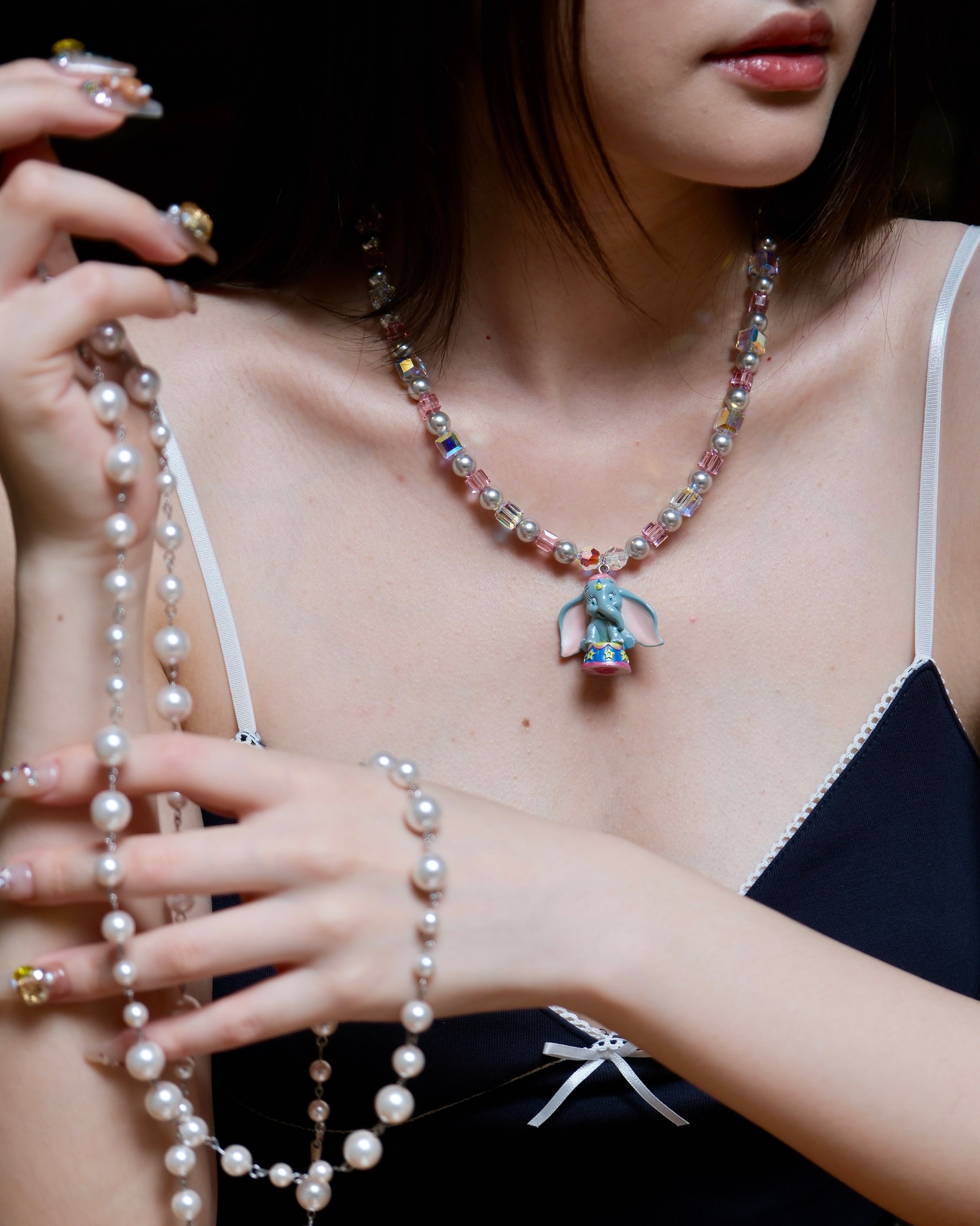 Close-up of a handmade blue elephant charm necklace with gray Swarovski pearls, pink beads, and iridescent crystal accents.