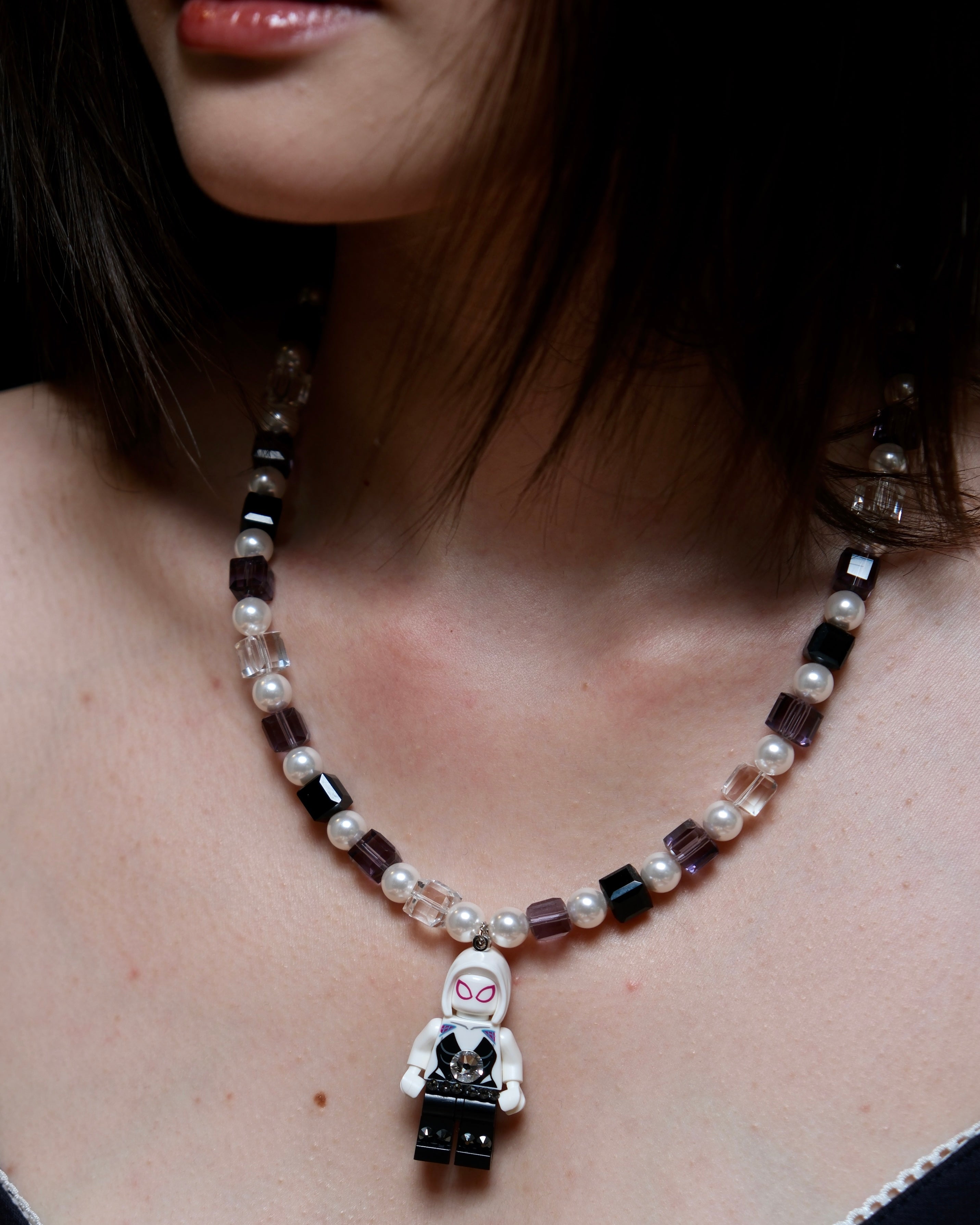 Close-up of a handmade pastel crystal charm necklace with white pearl accents and a playful vintage-inspired pendant.