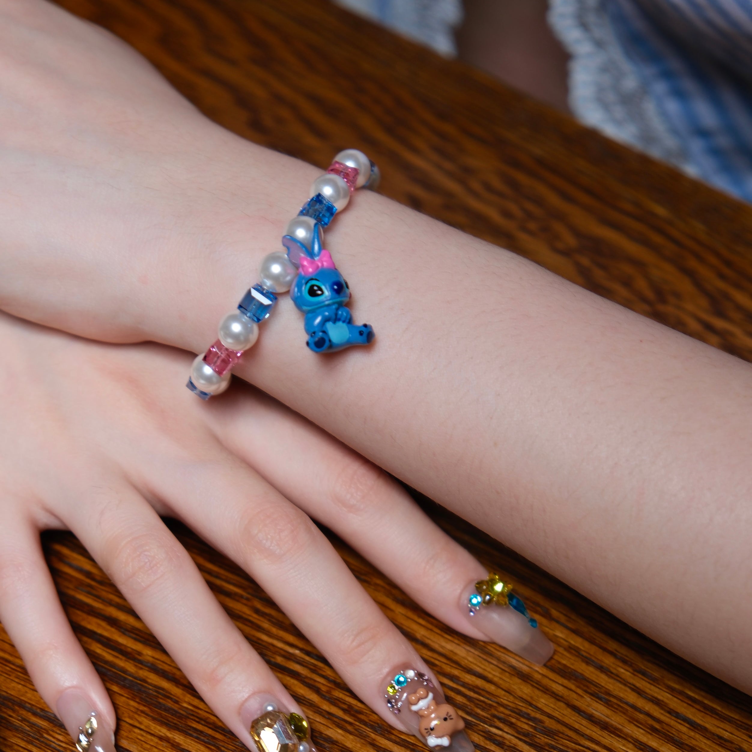 Model wearing a handmade blue charm bracelet with white pearls, blue and pink crystal beads, and a playful bow charm.