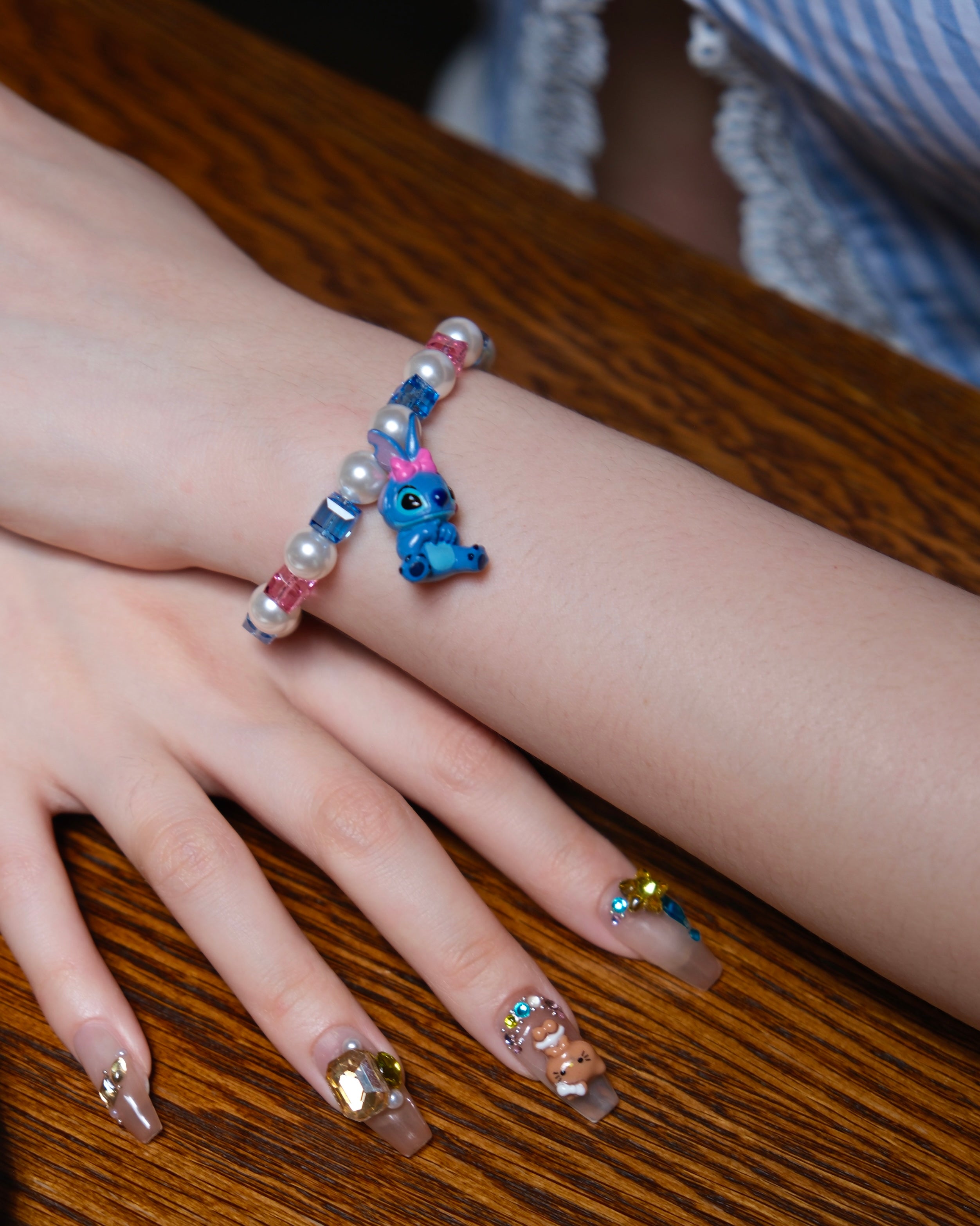Model wearing a handmade blue charm bracelet with white pearls, blue and pink crystal beads, and a playful bow charm.