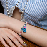 Close-up of a handmade blue charm bracelet with white pearls, blue and pink crystal beads, and a playful bow charm.
