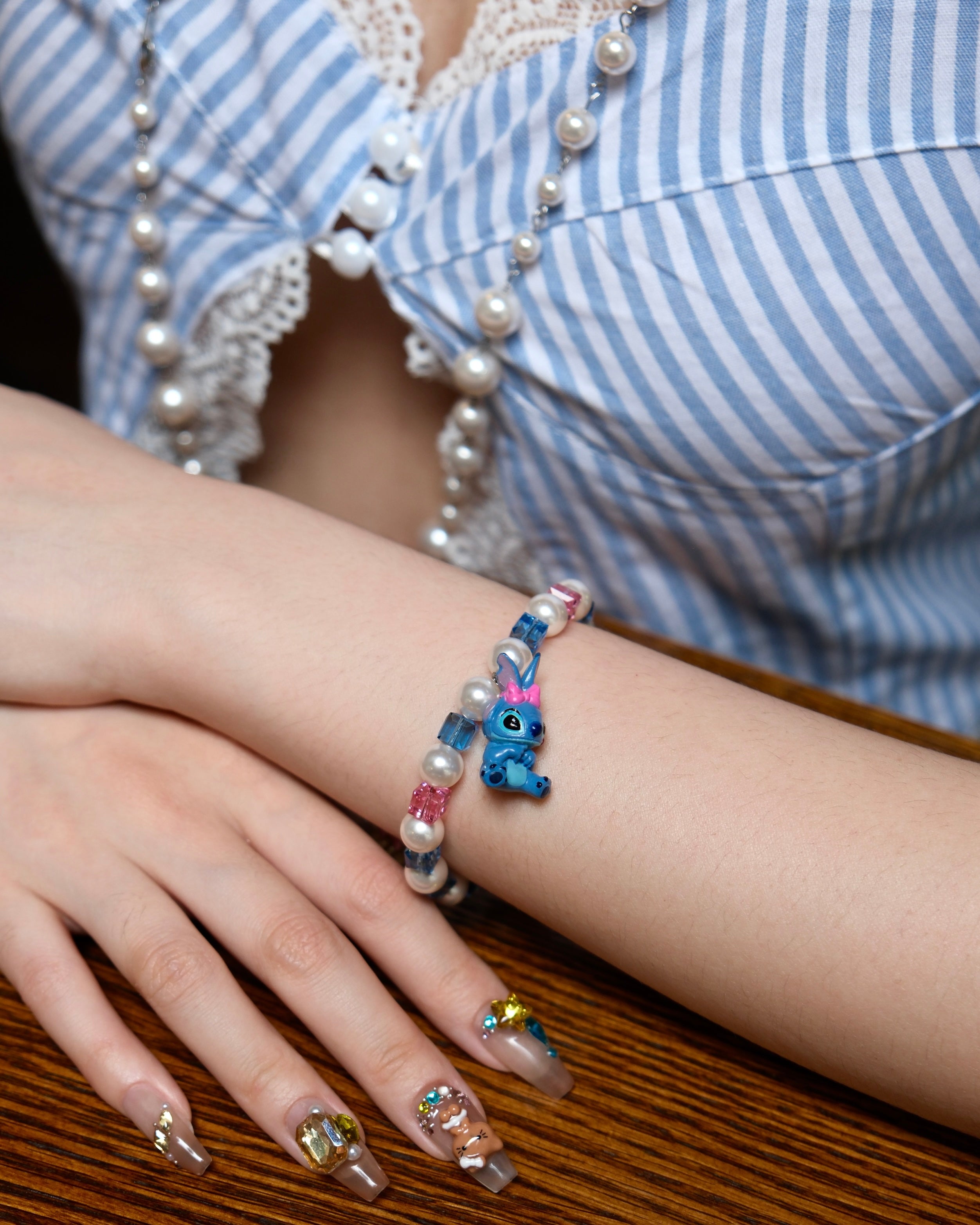 Close-up of a handmade blue charm bracelet with white pearls, blue and pink crystal beads, and a playful bow charm.
