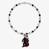 Studio product photo of a handmade black pearl charm necklace with Swarovski crystal beads and a vintage-inspired cello-player pendant.